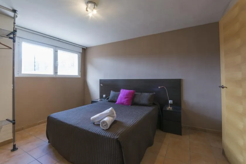 A bedroom with a dark bed, colorful pillows, and a window.