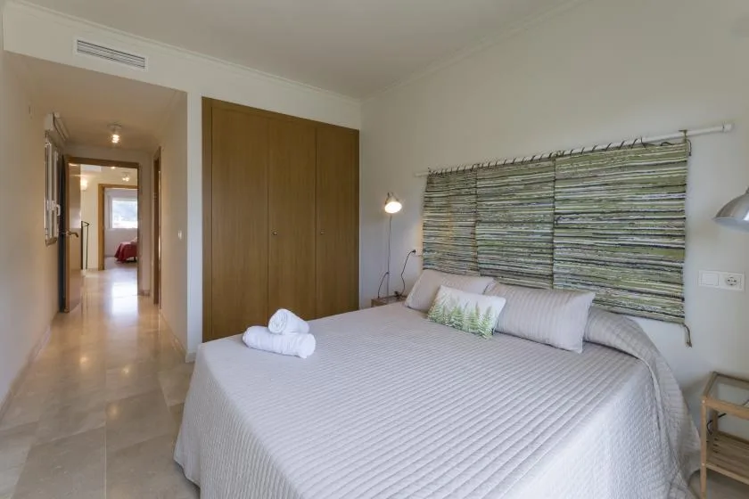 A bedroom with a neatly made bed beneath a wide window shade.