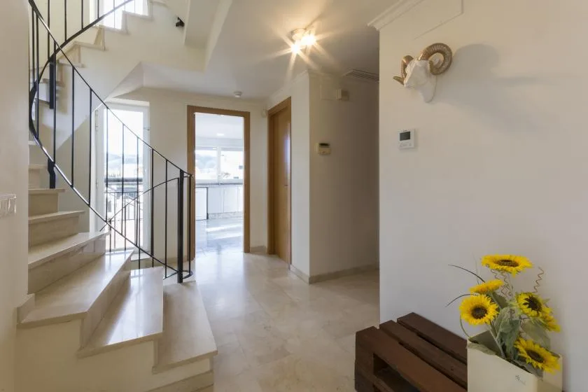 An interior hallway with a staircase and a doorway opening into a bright room.