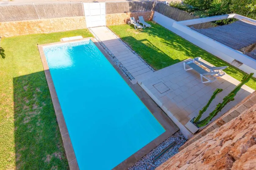 Una piscina rectangular está junto a un patio embaldosado y un césped verde.