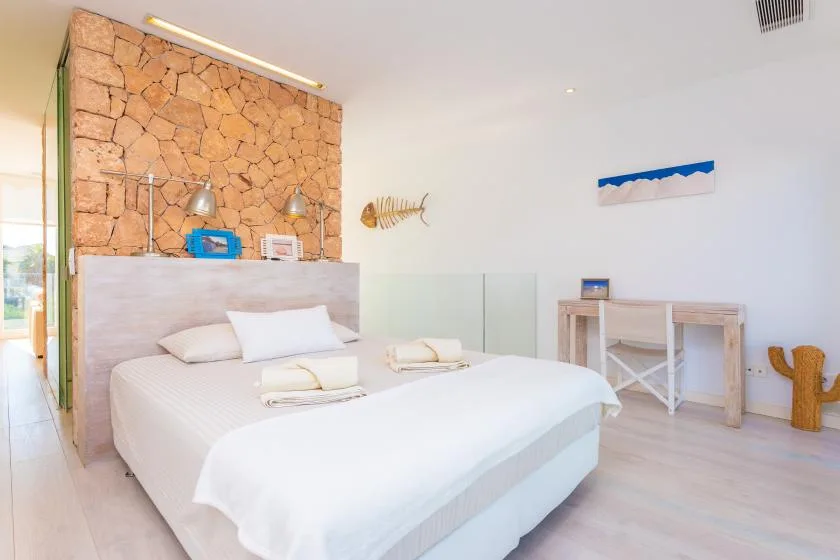 Un dormitorio luminoso con una cama, una pared de piedra decorativa y un escritorio pequeño.