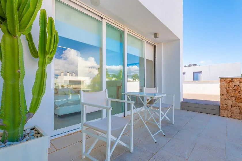 Un pequeño patio exterior con una mesa blanca y sillas junto a grandes puertas de vidrio.