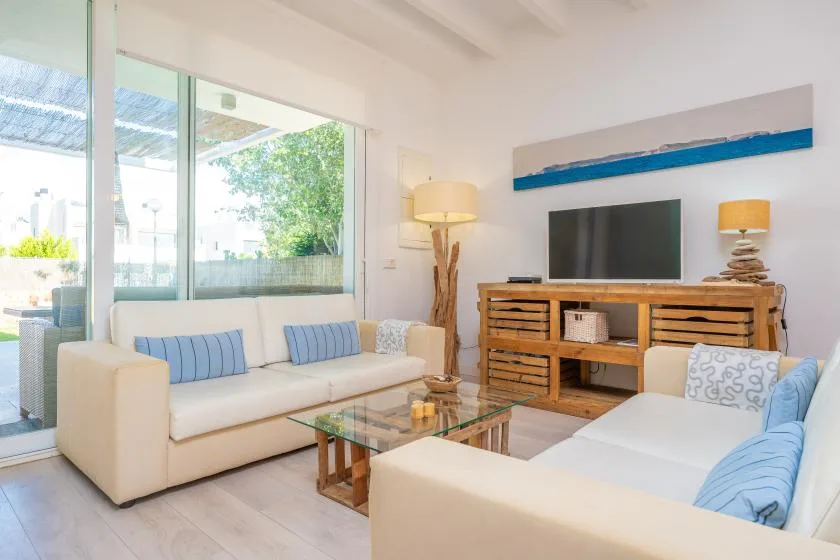 A bright living room with seating, a glass coffee table, and a television.