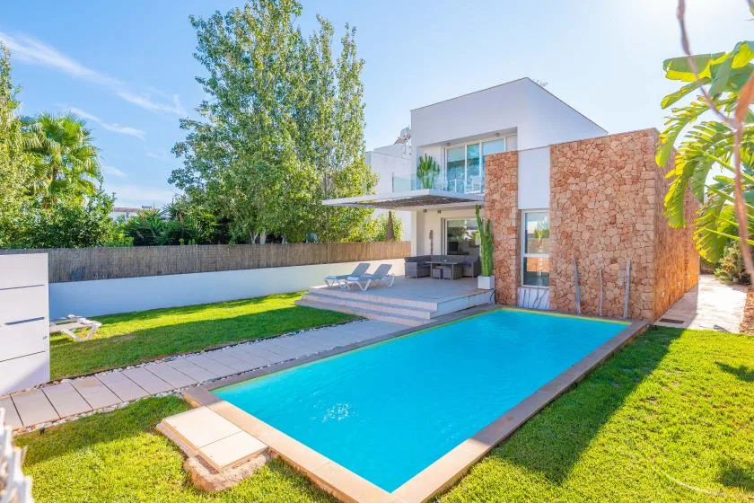 A modern house with a rectangular swimming pool, lawn, and outdoor seating.