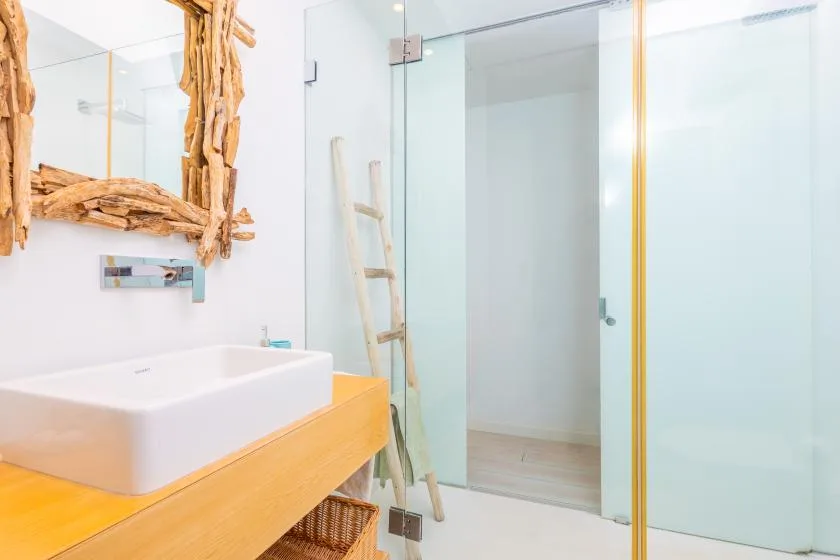Un baño luminoso con lavabo sobre encimera, ducha de vidrio y espejo con marco de madera.