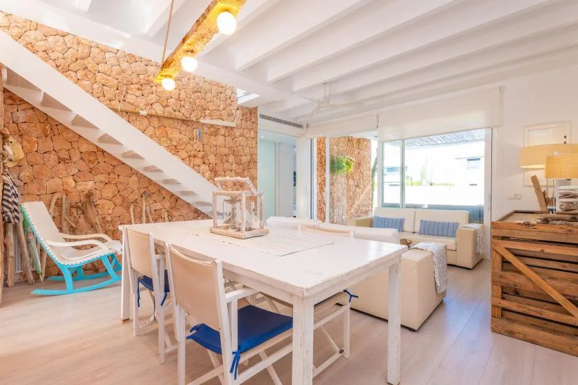 Una luminosa zona de comedor y estar tiene una mesa larga junto a una pared de piedra.