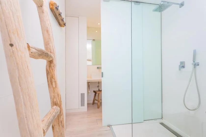 Un baño luminoso con una ducha de cristal y un lavabo visible a través de la puerta.