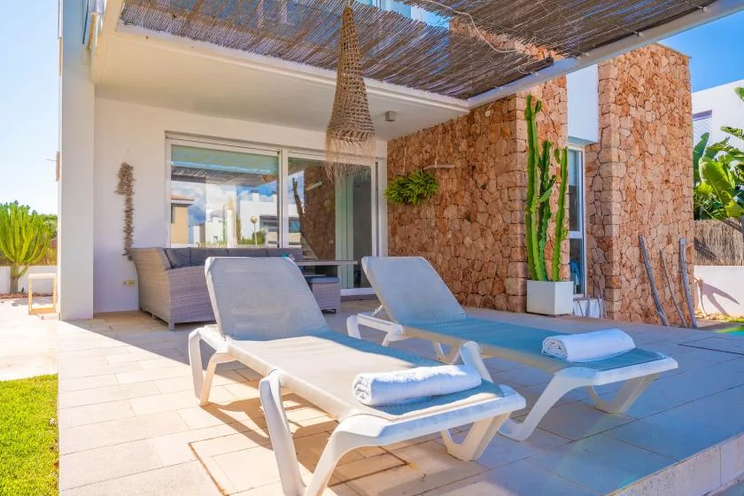 Un patio soleado con asientos reclinables junto a una pequeña piscina.