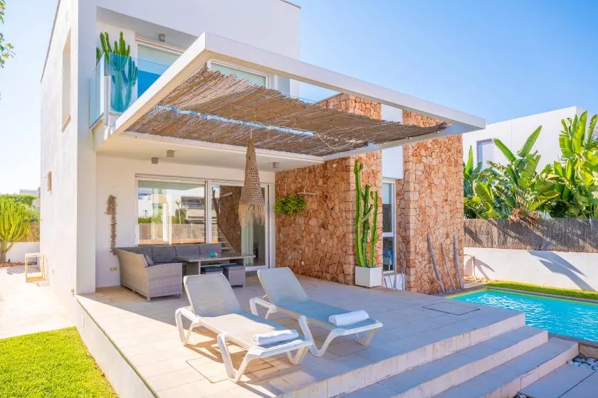 Una piscina exterior junto a un patio sombreado con asientos.