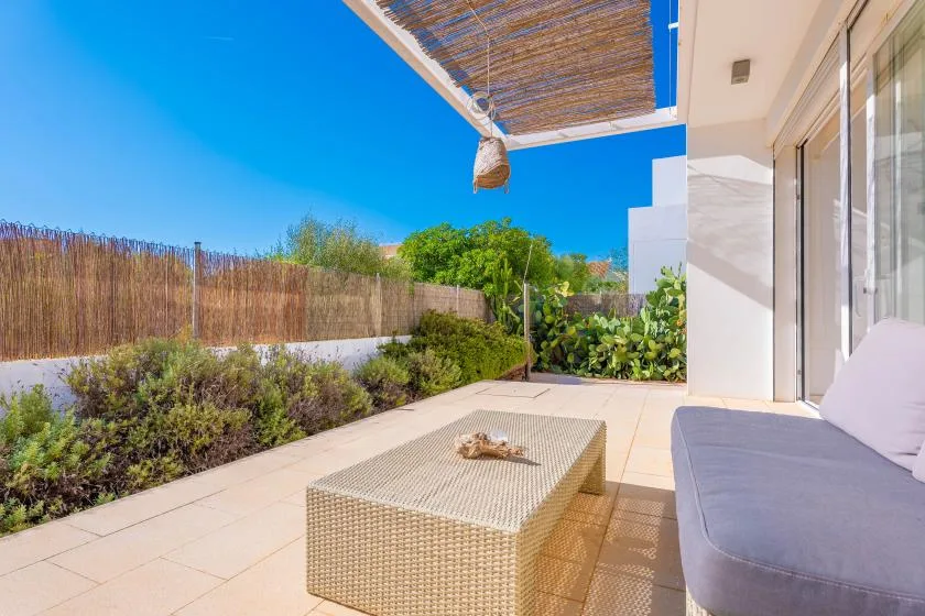 Un patio soleado con asientos al aire libre, una mesa baja y plantas verdes.