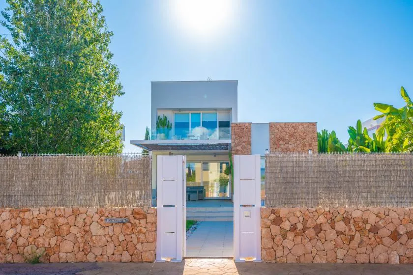 Entrada de una casa moderna con puerta blanca, muro de piedra y vegetación.
