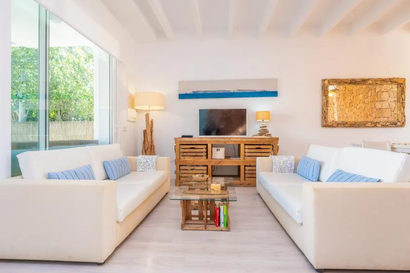 Una luminosa sala de estar con asientos blancos frente a un televisor y un mueble de madera.