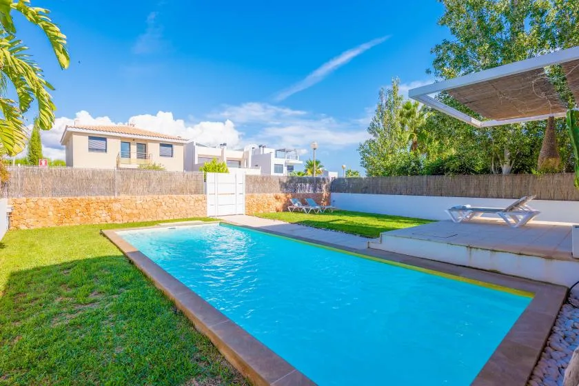 Piscina exterior con césped y una zona de estar sombreada.