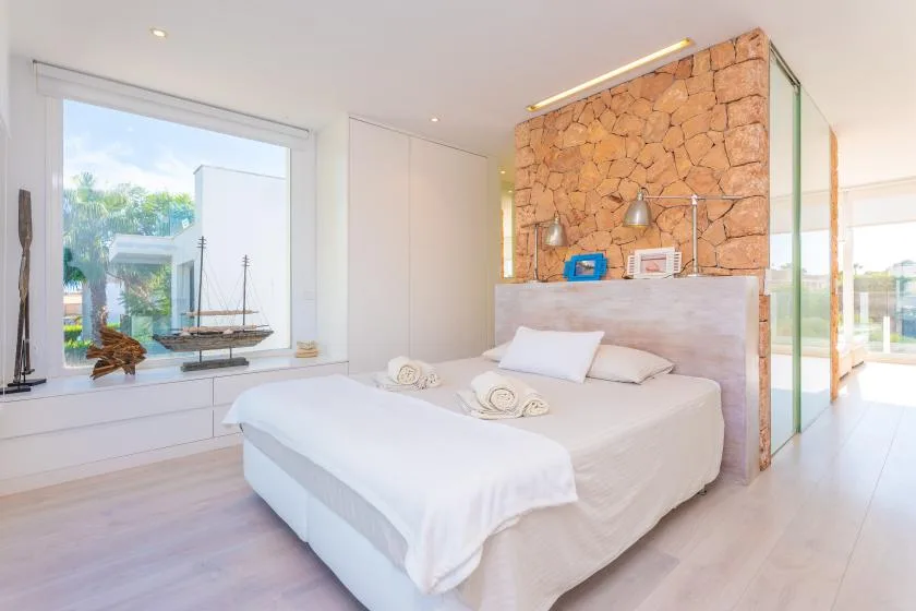 Un dormitorio luminoso con una cama junto a una ventana grande y una pared de piedra.