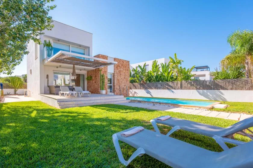 Una casa moderna da a una piscina, con césped y tumbonas en primer plano.