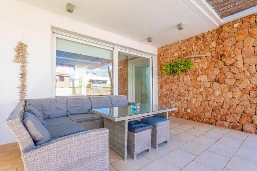 A covered patio has a seating area and a table beside a stone wall.