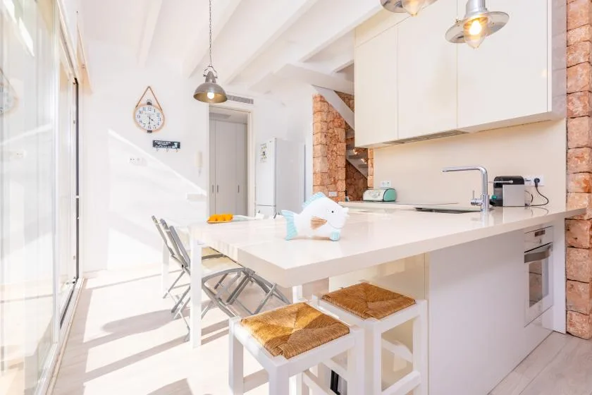 Una cocina luminosa con una isla blanca, taburetes y un fregadero.