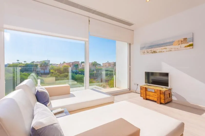 Una sala de estar luminosa con asientos junto a grandes ventanales y vistas a una zona ajardinada.