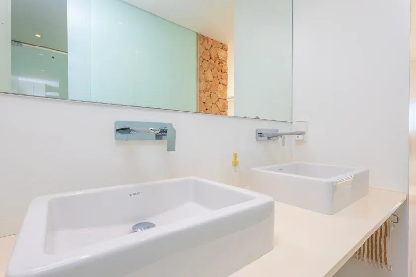 Un tocador de baño con dos lavabos blancos sobre la encimera y grifos de pared.