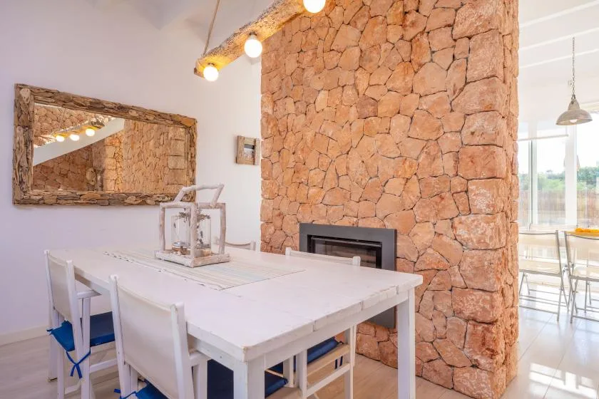 Un comedor luminoso con una mesa blanca junto a una pared de piedra.