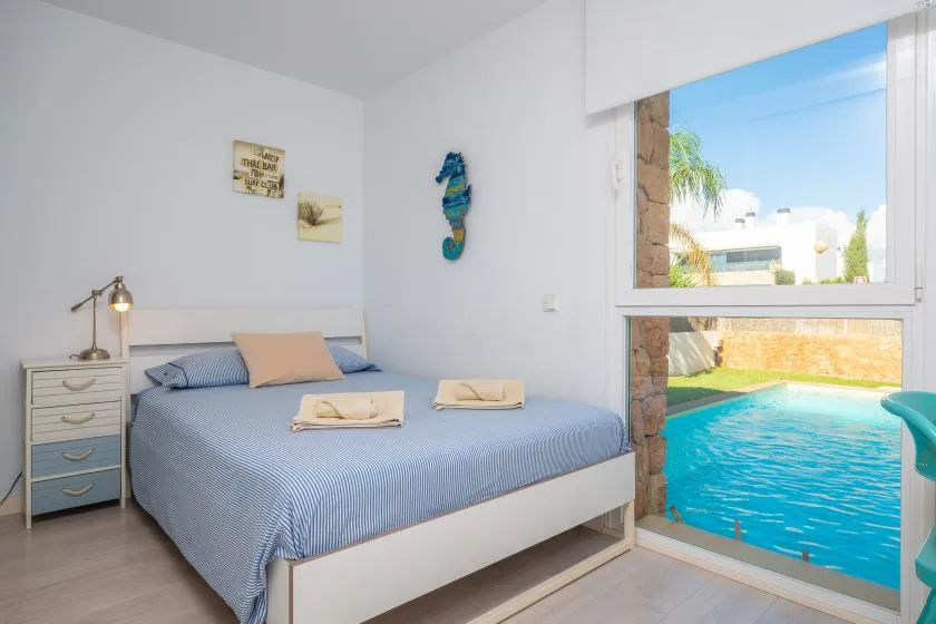 Un dormitorio con una cama tendida junto a una gran ventana con vistas a una piscina.