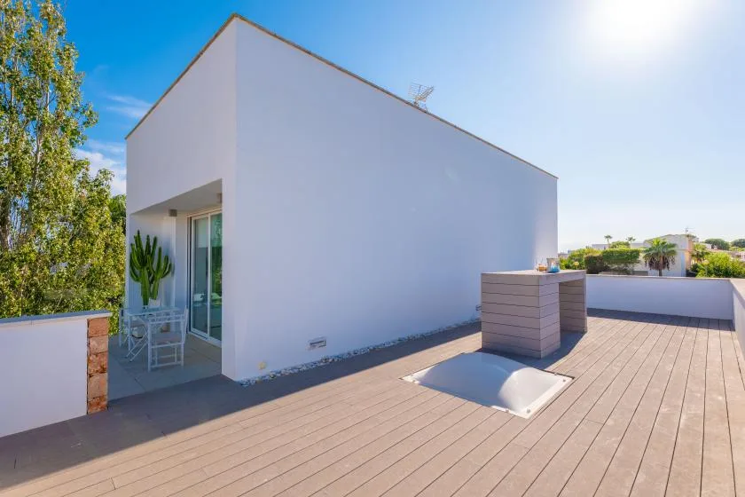Una terraza soleada en la azotea con un edificio blanco y suelo de madera.