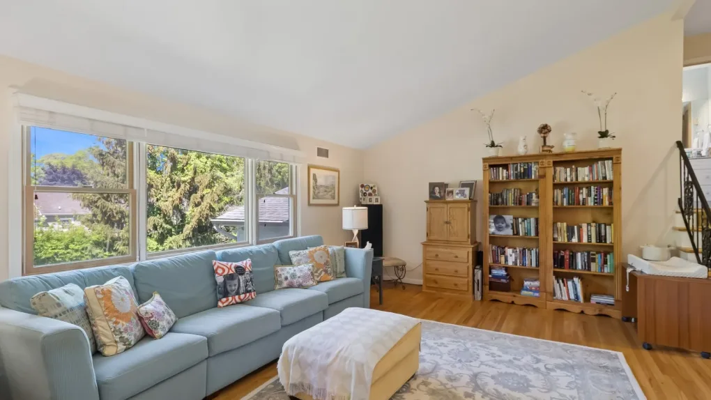 Una sala luminosa con un sofá azul, una estantería y grandes ventanas.