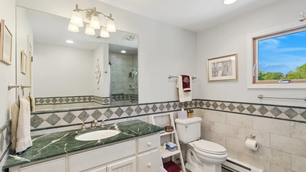 Un baño luminoso con una encimera verde y una ventana con vistas a la vegetación.