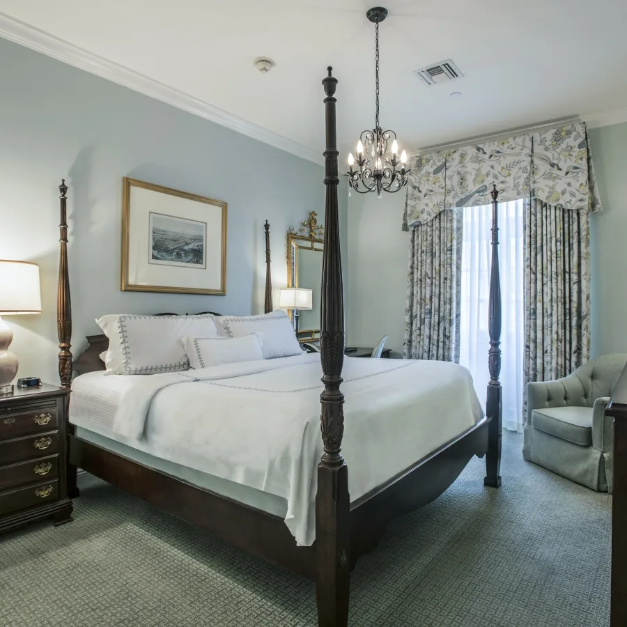 Deluxe King room with a four-poster bed, armchair and patterned curtains.