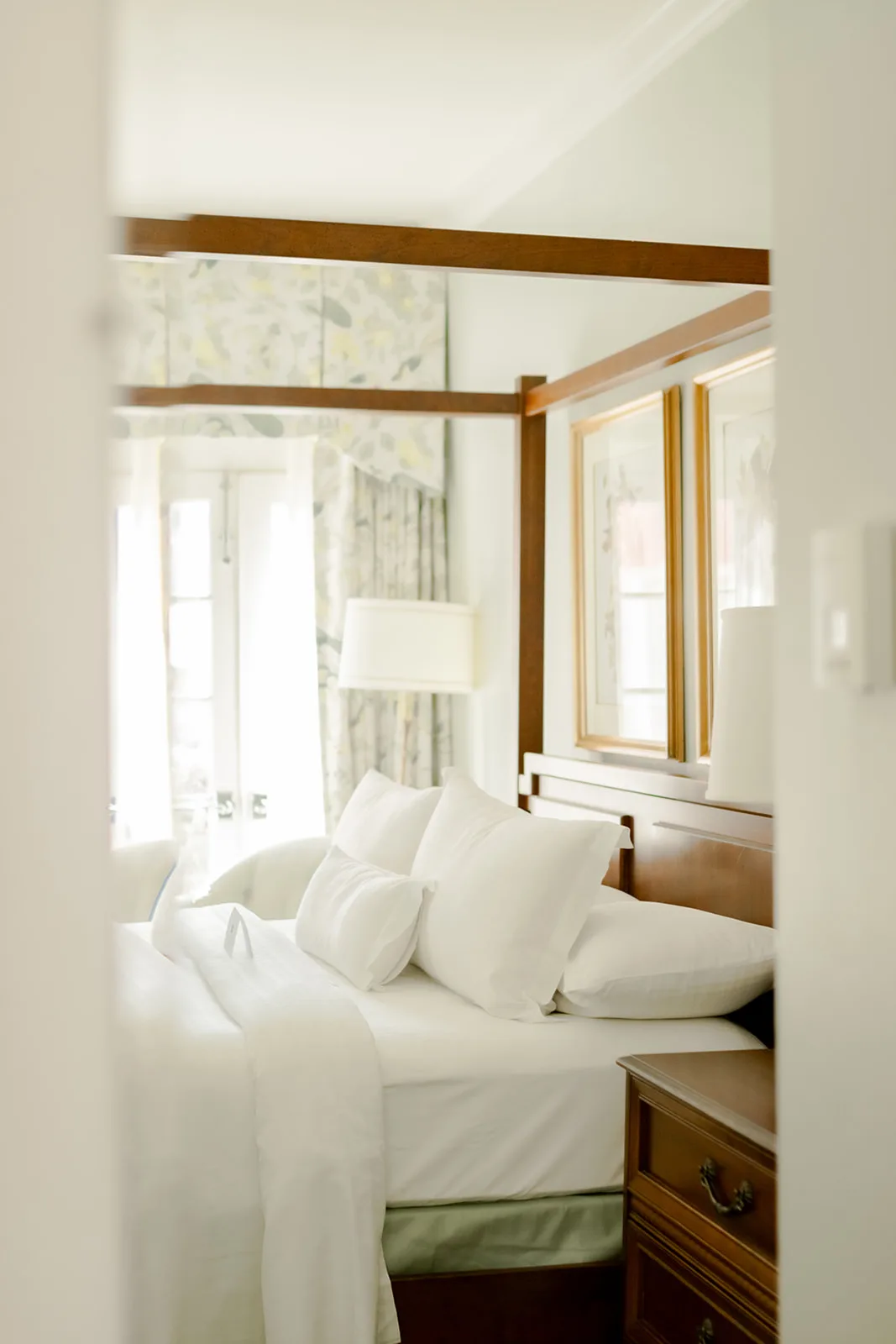 Hotel room bed and carved wooden bedposts viewed from the hallway entrance.