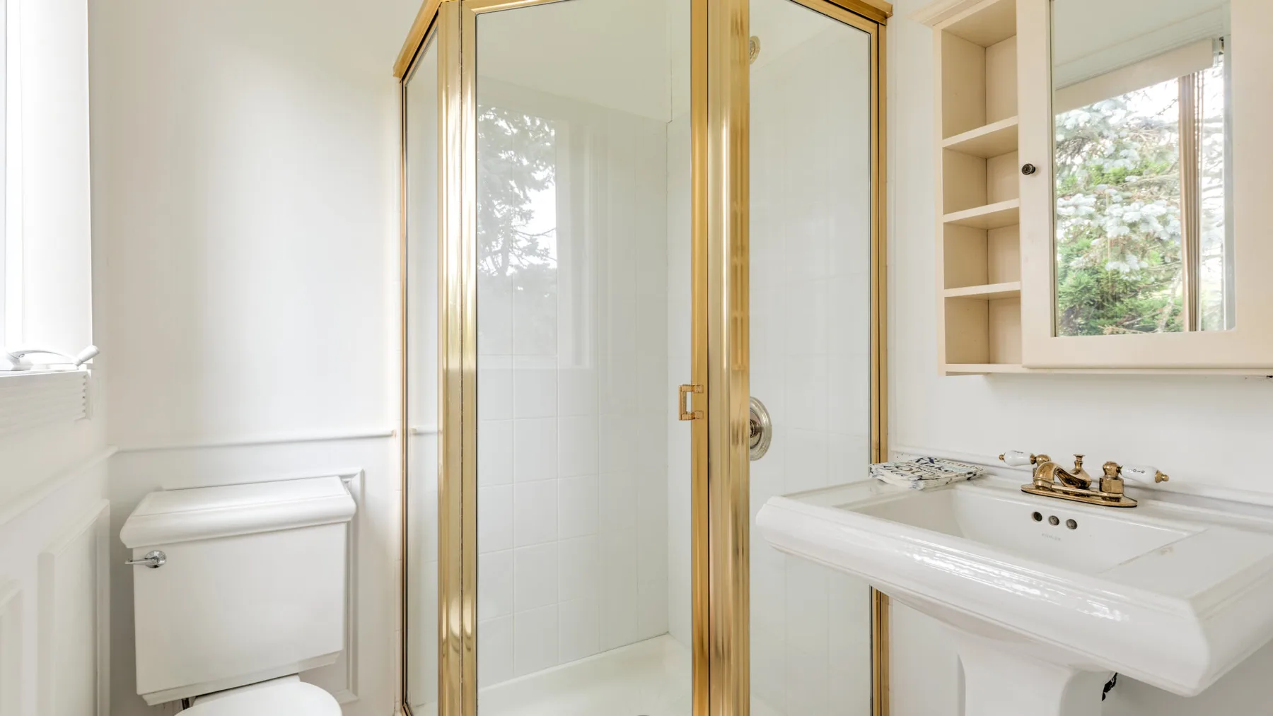 A bathroom with a glass shower enclosure and a sink beneath a window.