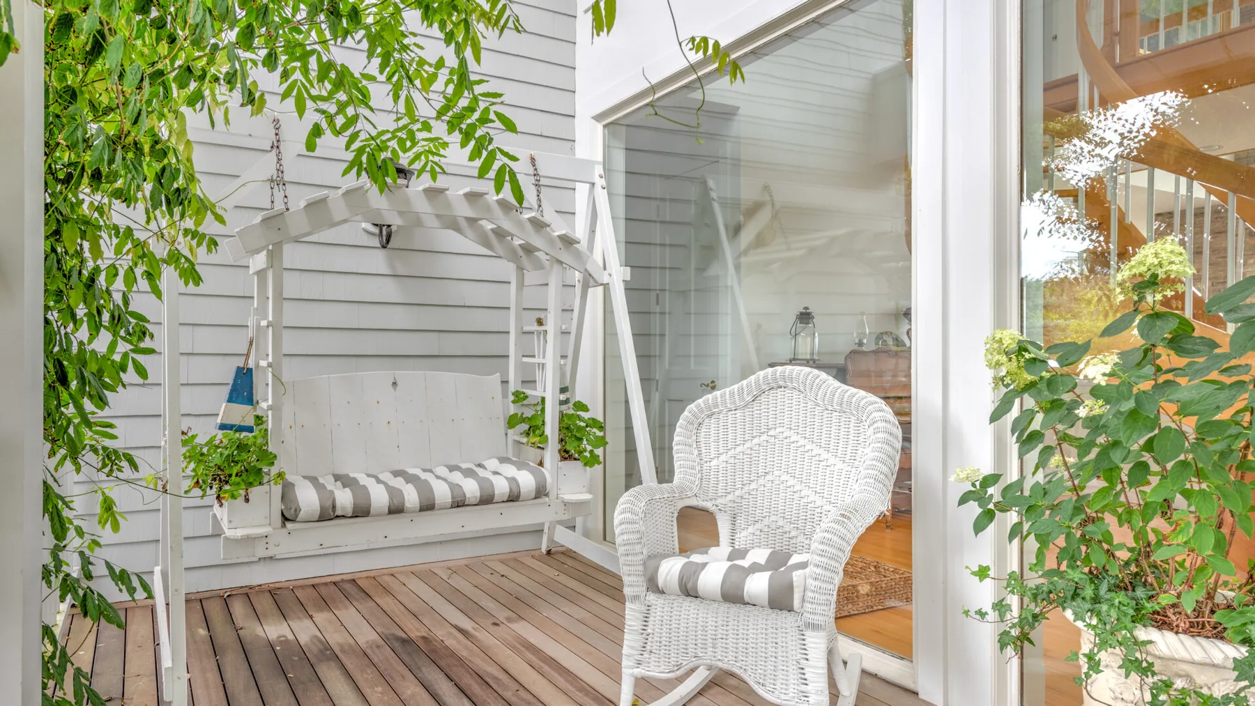 A small outdoor seating area has a wooden deck, cushioned swing, and wicker chair.