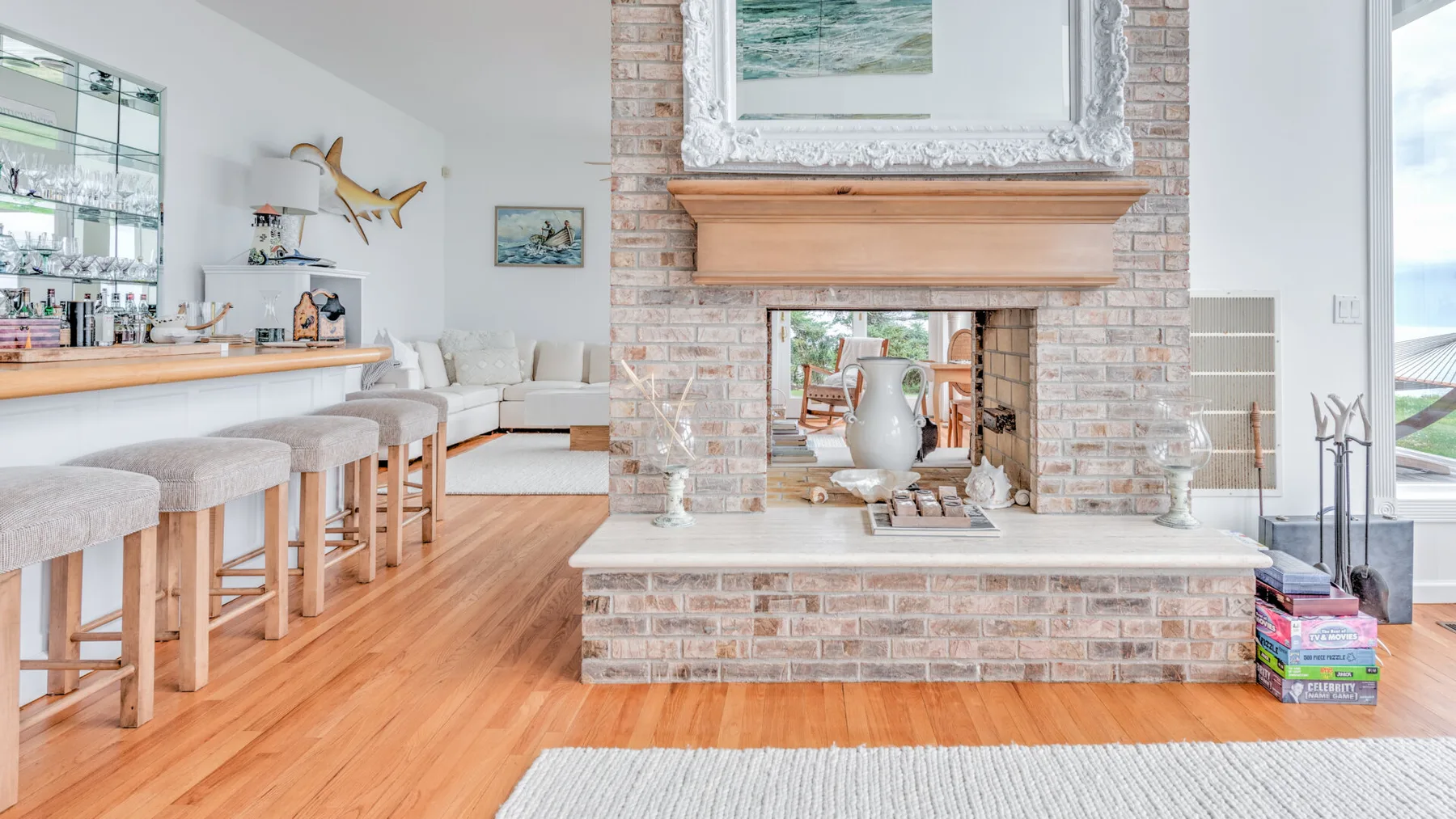 A bright living room with a brick fireplace and a bar counter with stools.