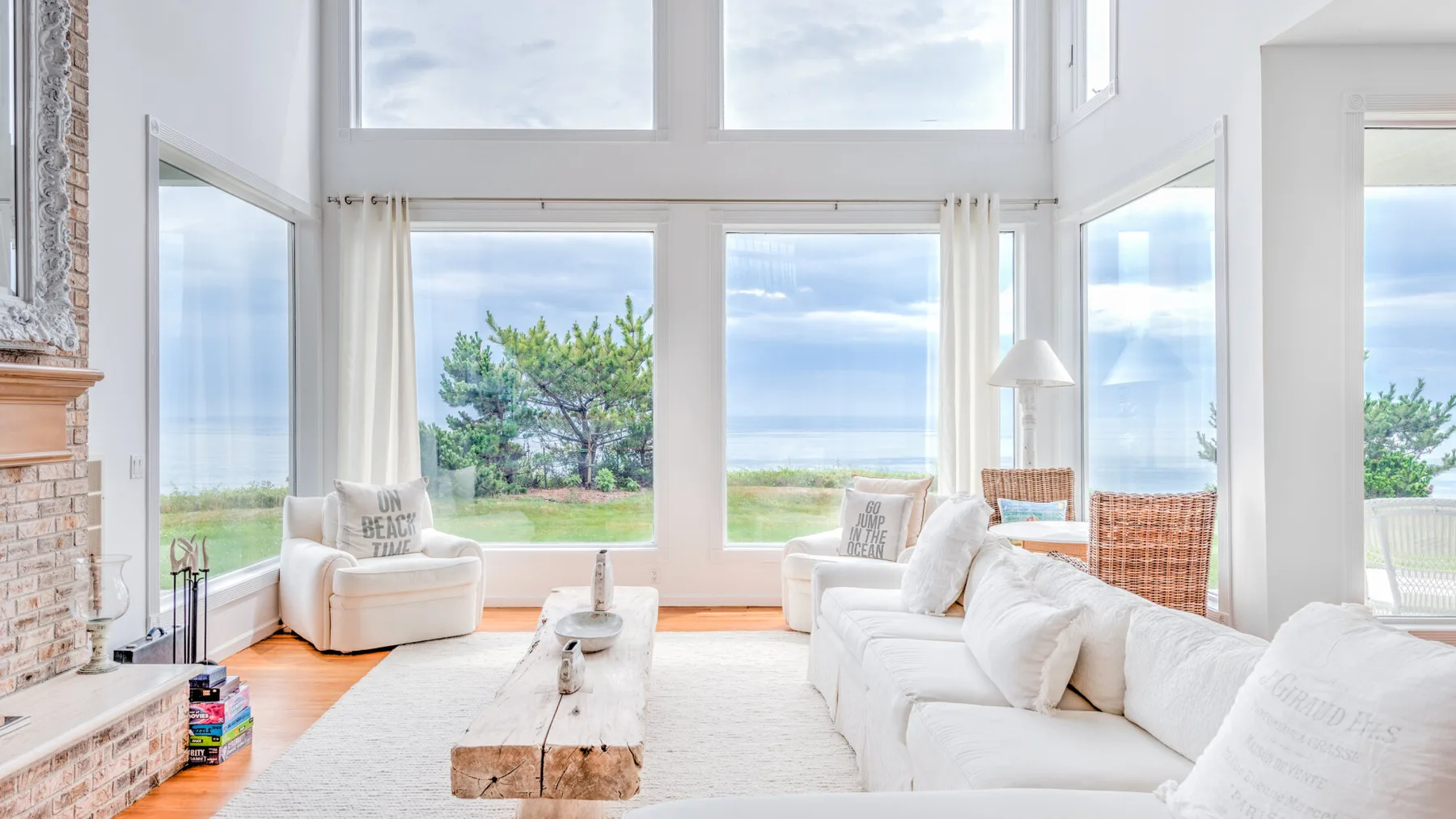 A bright living room with white seating and large windows overlooking the water.
