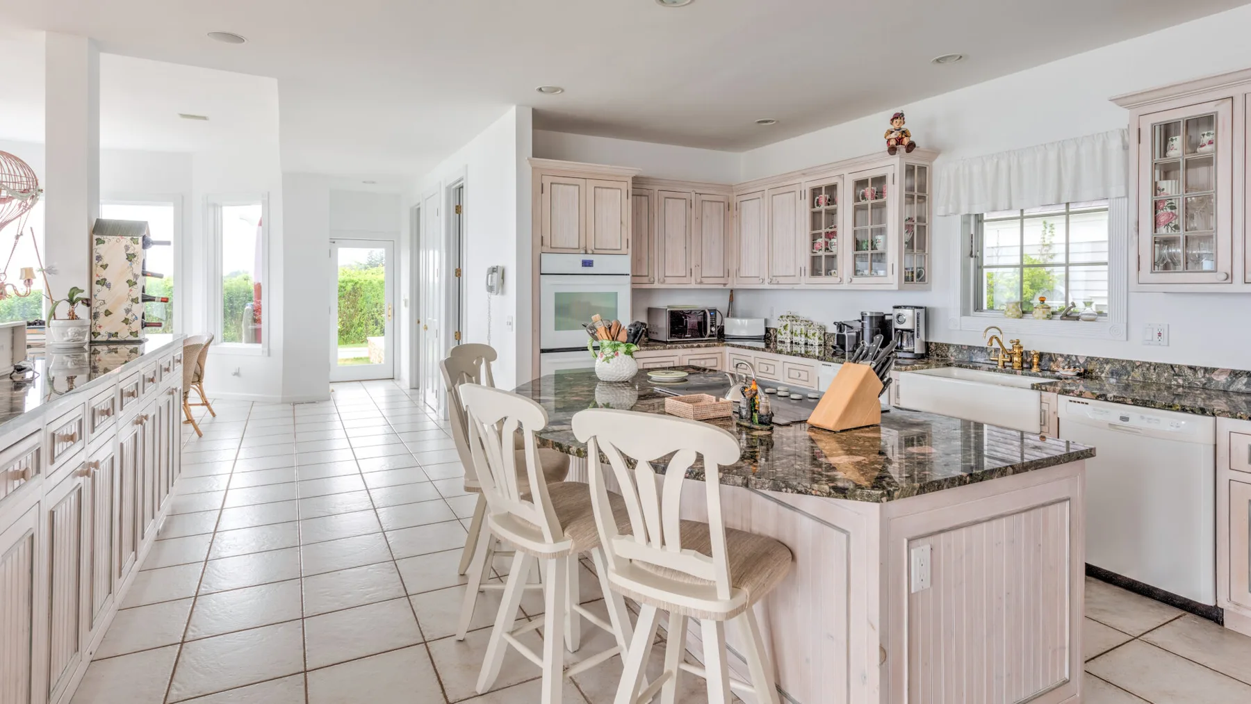 A bright kitchen with pale cabinetry, dark countertops, and a central island with seating.