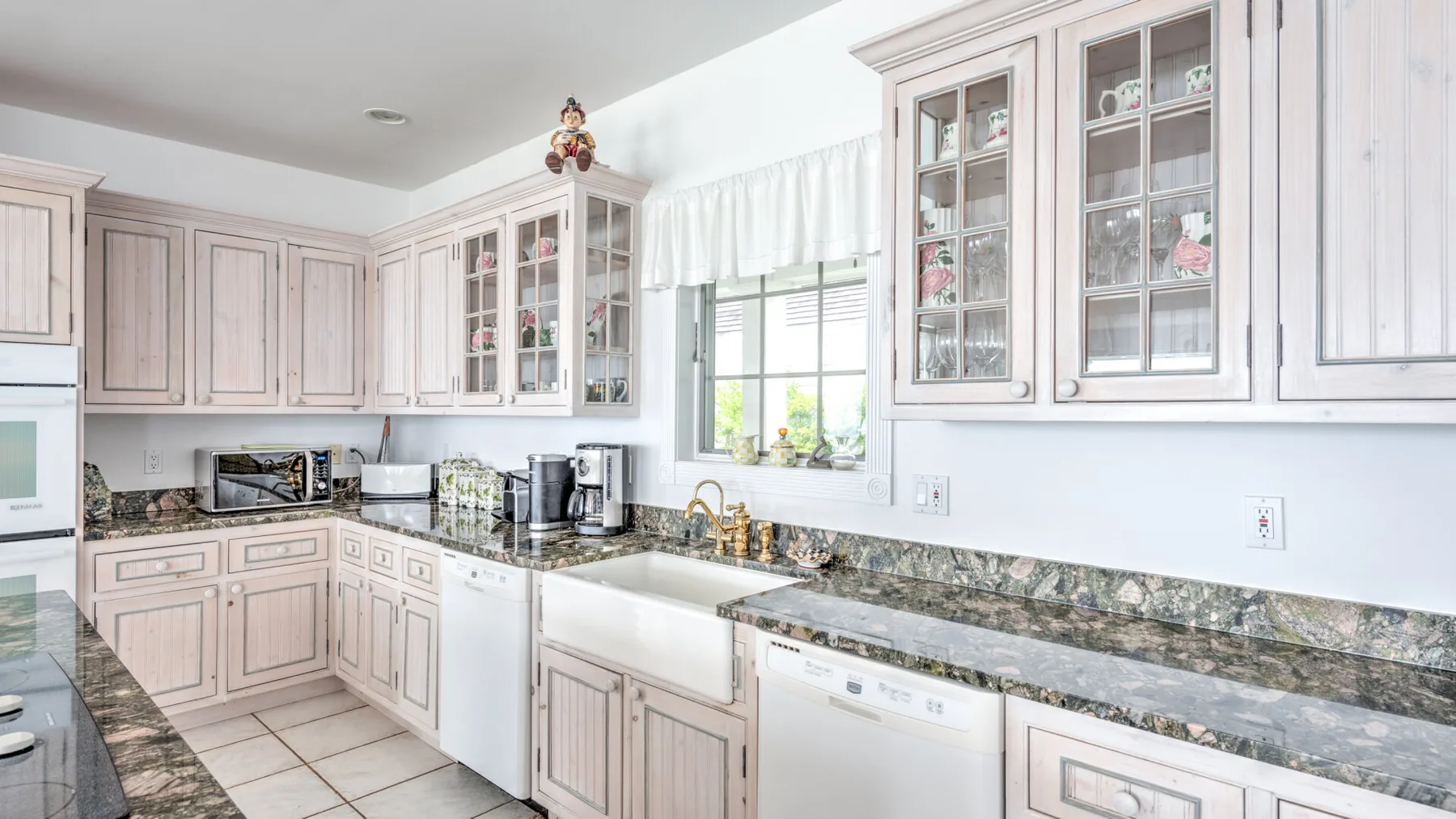 A bright kitchen with pale cabinetry, dark countertops, and a window above the sink.