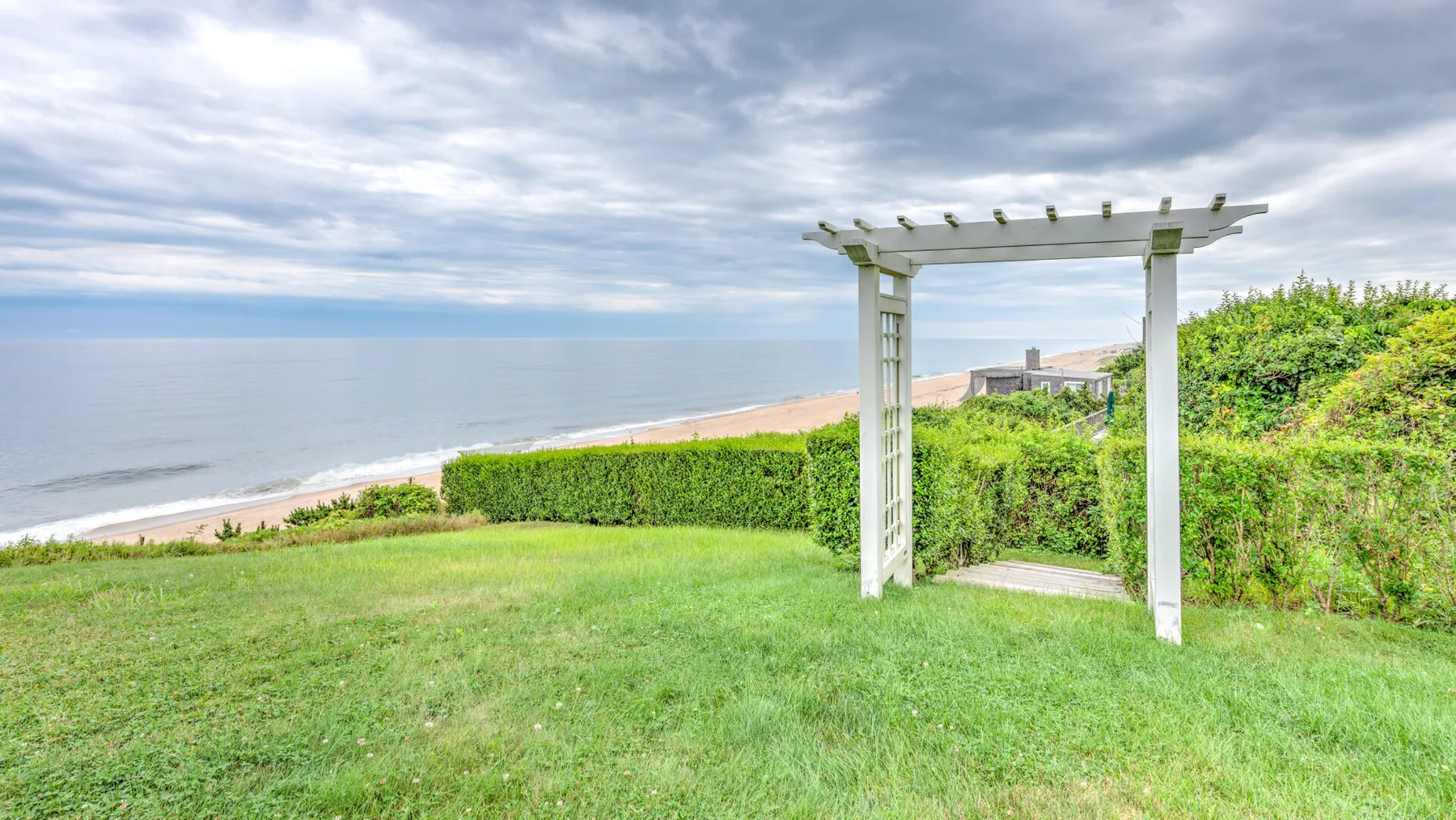 A grassy seaside lawn overlooks the ocean beside a white pergola.