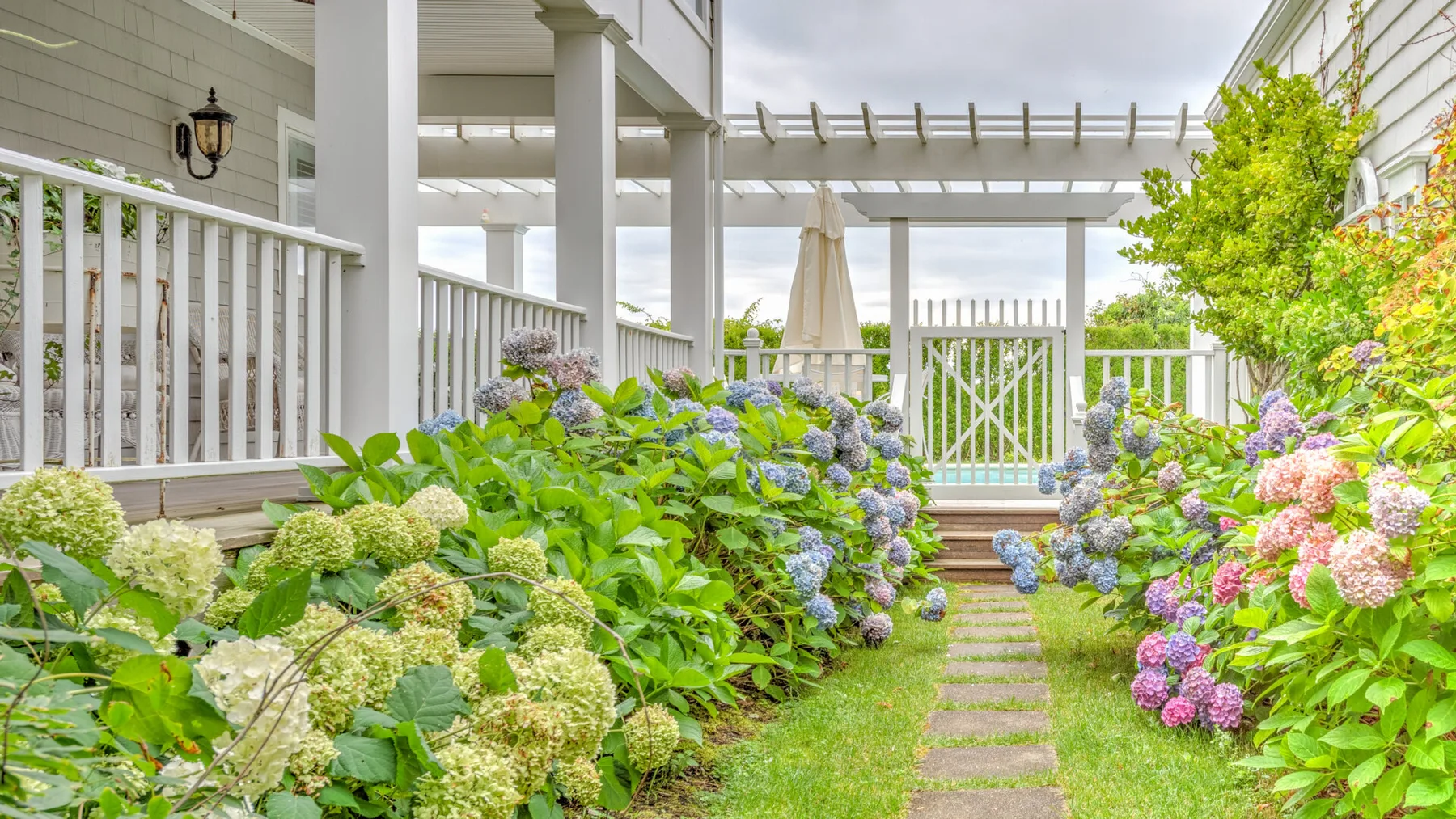 A garden path winds between flowering shrubs beneath a white pergola.