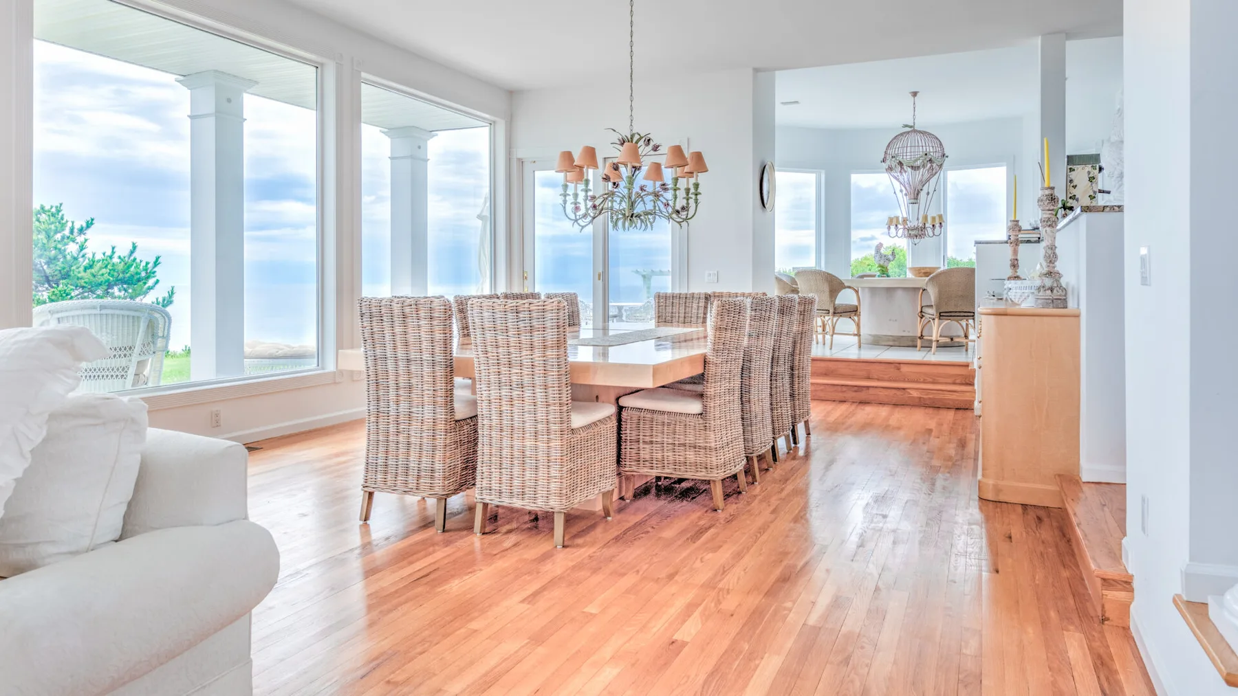 A bright dining area with a wooden table and woven seating beside large windows.