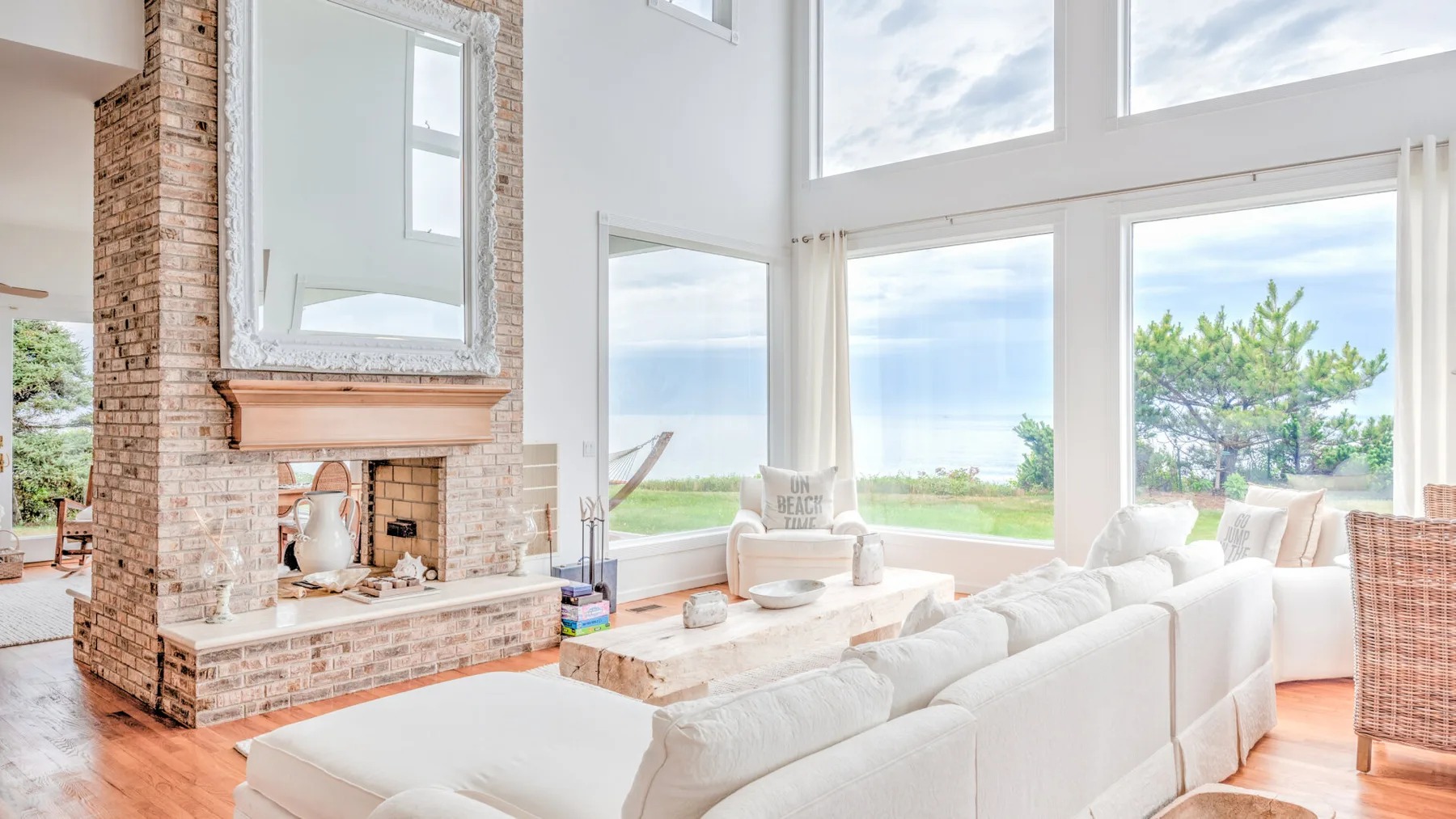 A bright living room with large windows and a brick fireplace.