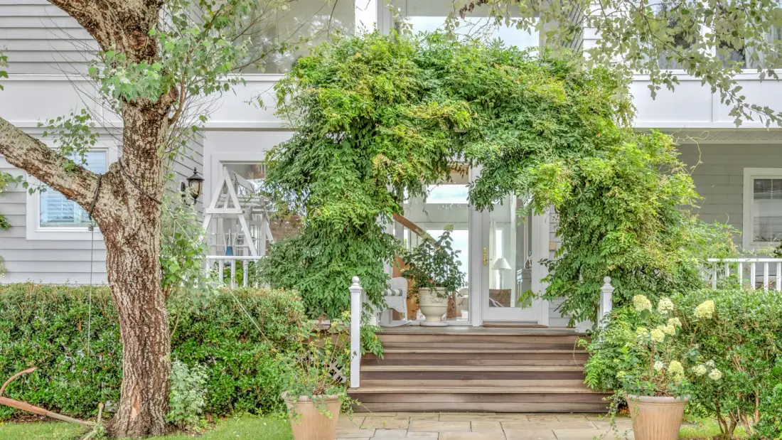 A leafy garden arch frames the steps leading to a house entrance.