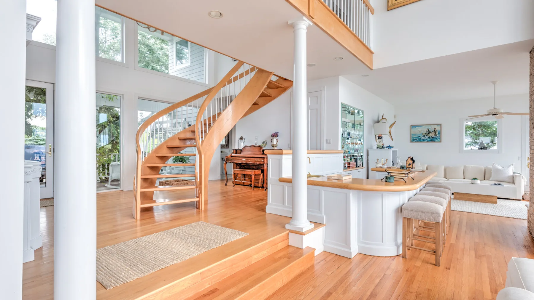 A bright open-plan living area features a curved wooden staircase and kitchen island.