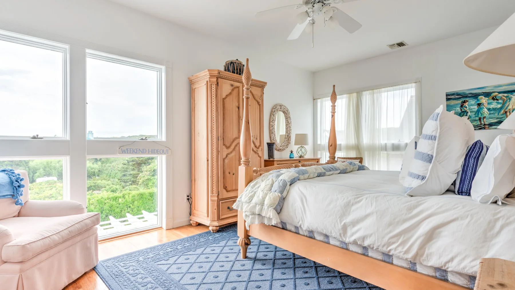 A bright bedroom with a large bed, an armoire, and windows overlooking greenery.