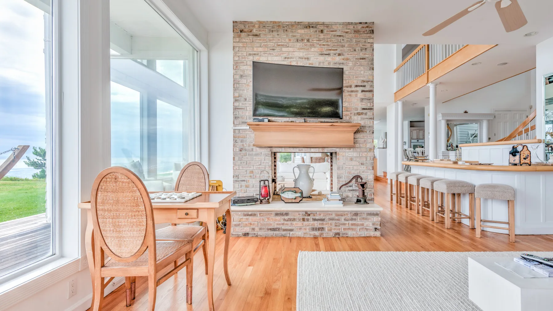 A bright open-plan living and dining area with tall windows and a brick fireplace.