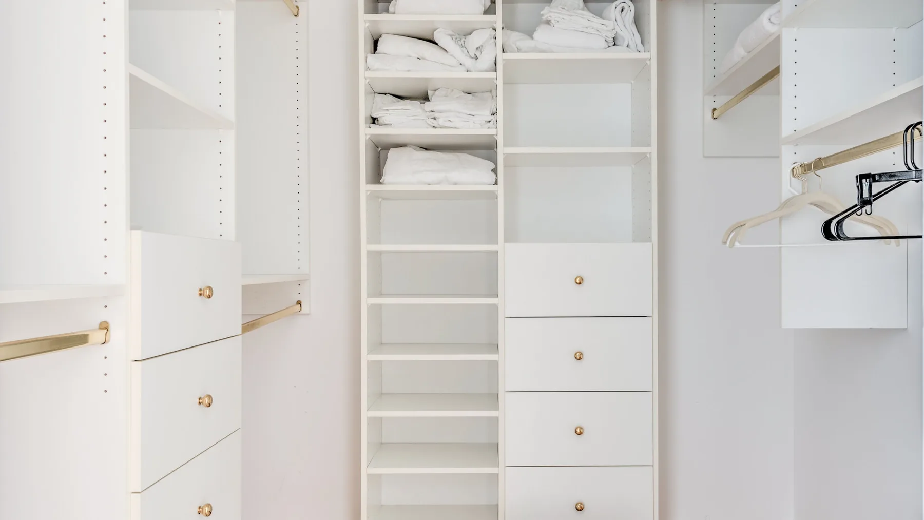 A white walk-in closet with open shelving, drawers, and hanging rails.