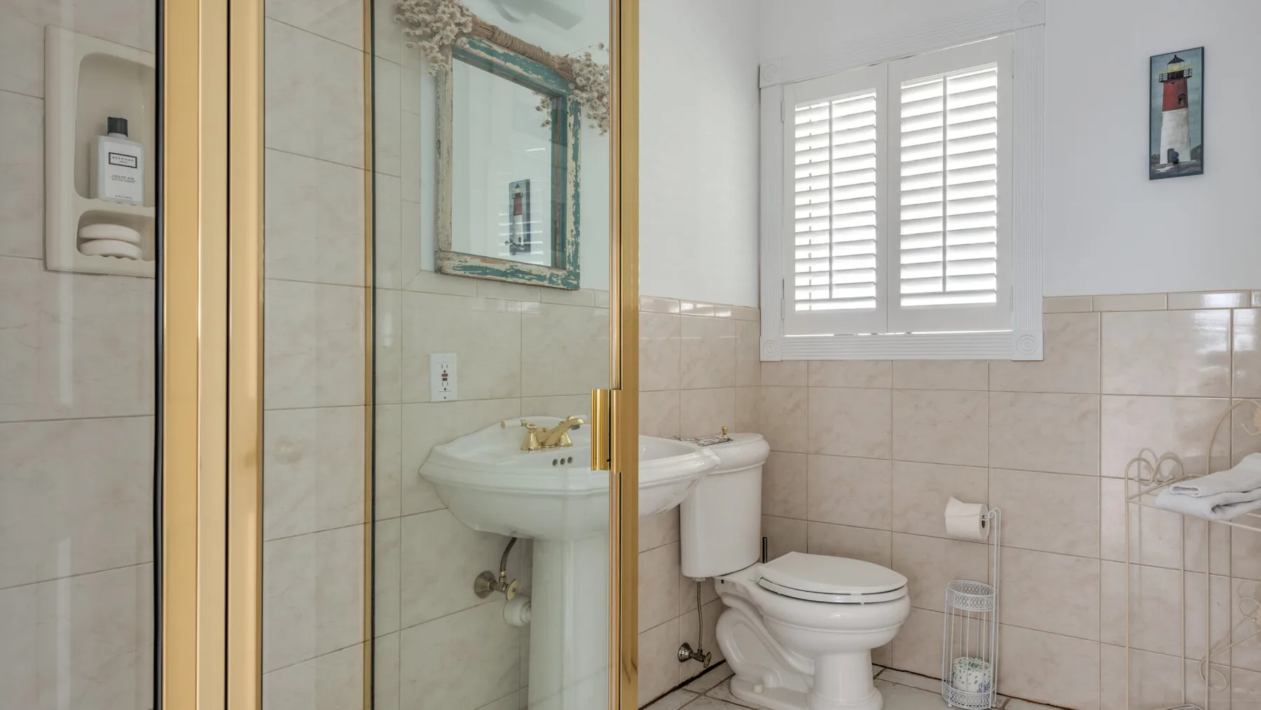 A tiled bathroom with a sink, toilet, and window with shutters.
