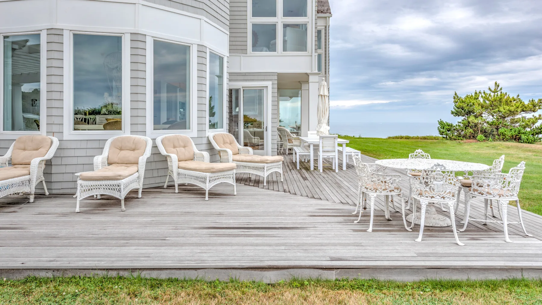 A seaside house has a spacious wooden deck with outdoor seating and a dining table.