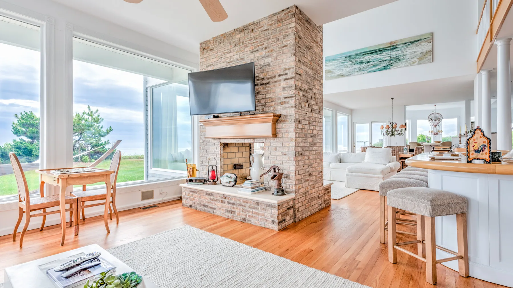 A bright open living area with a brick fireplace, large windows, and a dining table.