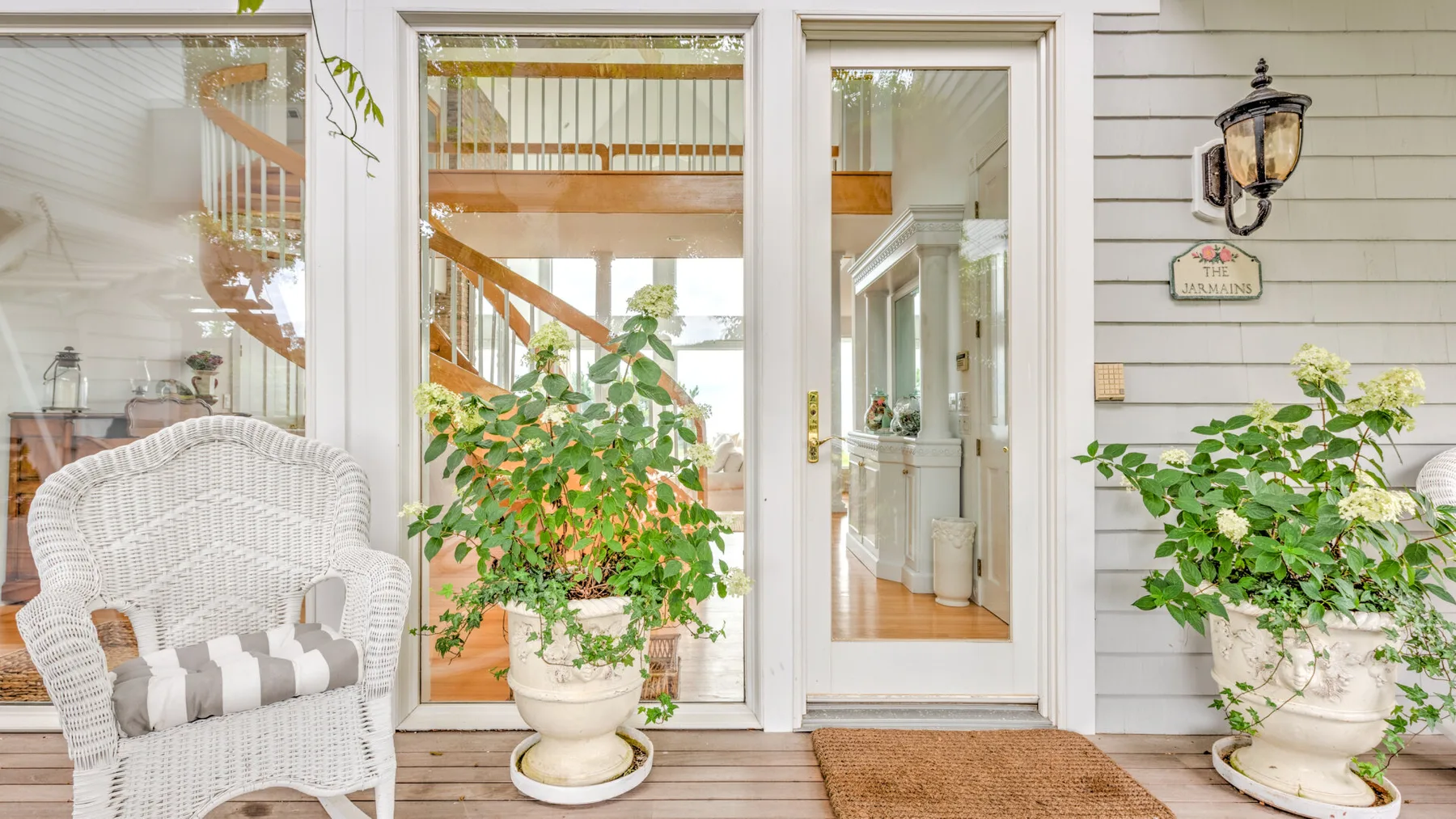A bright porch area with a wicker seat, potted plants, and glass doors.