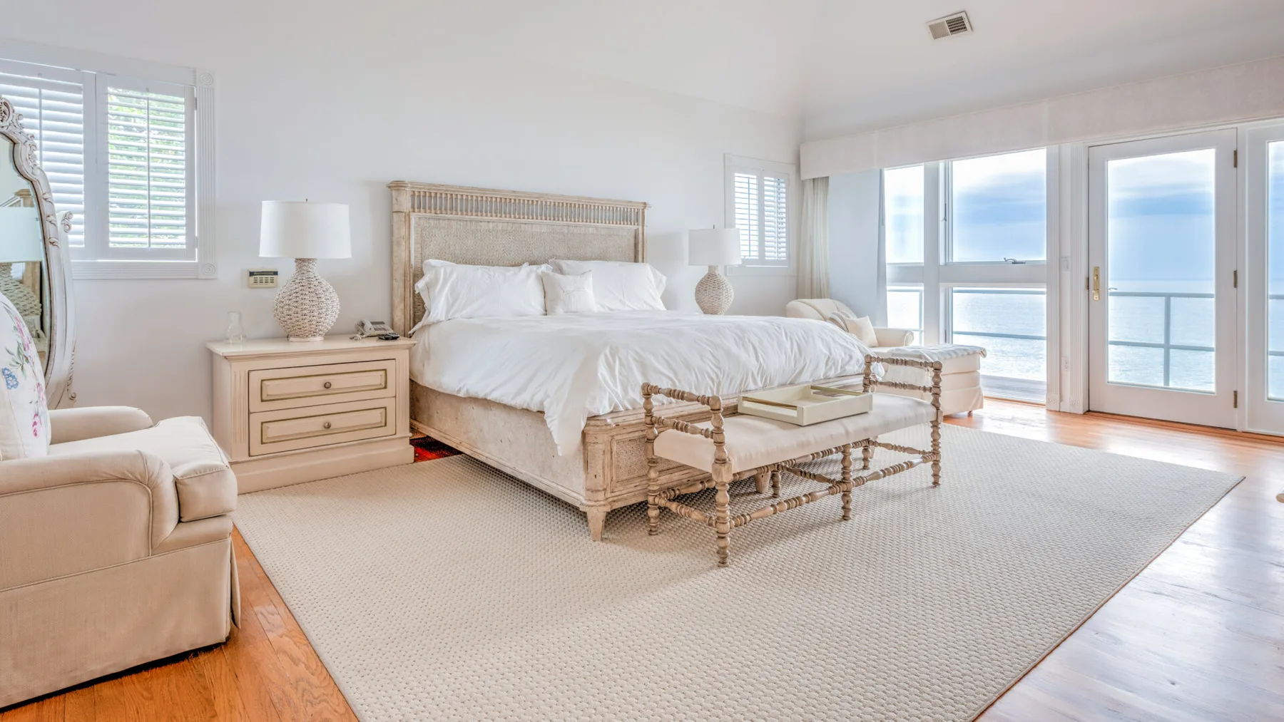 A bright bedroom with a large bed and windows overlooking the water.